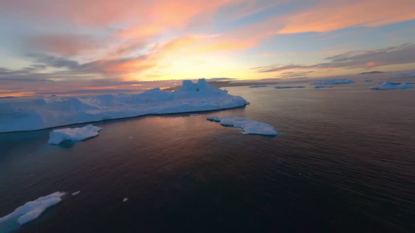 Breathtaking aerial drone flight over massive icebergs in glacial ocean during vibrant sunset, showcasing natural beauty and serene arctic landscape, cinematic motion.