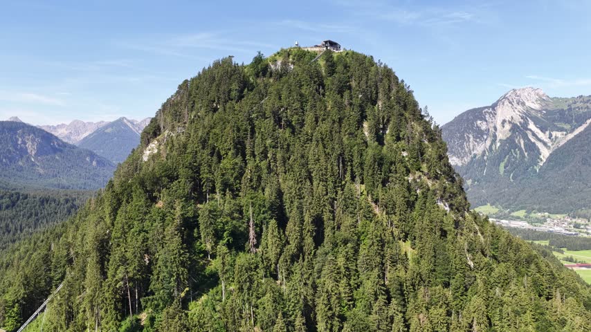Ehrenberg Castle ruins rise from a densely forested hill near Reutte, Austria, framed by layered Tyrolean peaks and a broad green Alpine landscape.