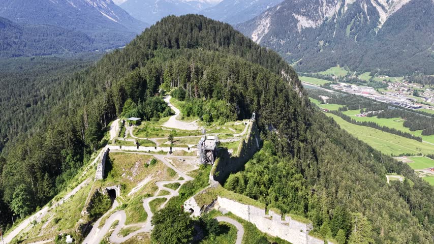 Close aerial view of Ehrenberg Castle ruins near Reutte, Austria, highlighting medieval stone walls and towers above a forested Alpine mountainside.