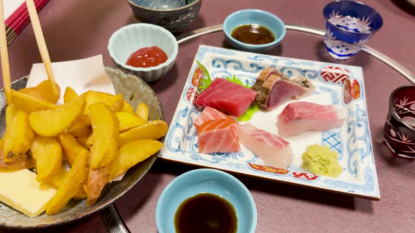 Close up of fried potato wedges with butter being dipped into tomato sauce beside fresh tuna salmon and yellowtail sashimi slices on traditional ceramic plate in restaurant setting.