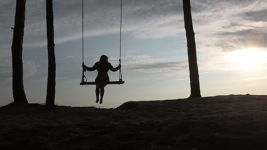 Silhouette of a Woman Swinging on a Rope Swing at Sunset by the Sea