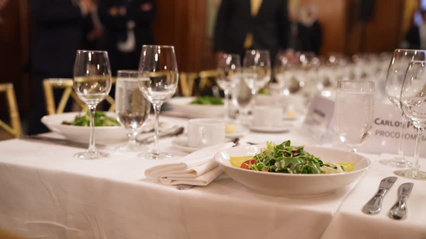 Elegant banquet dinner table setup with sparkling crystal glasses, fine dining plates, and professional catering at a luxury formal event or corporate gala.
