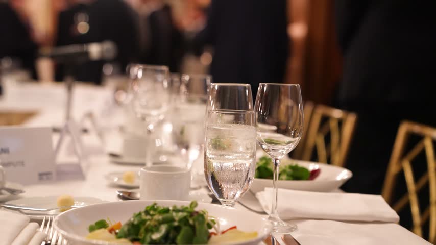Elegant banquet dinner table setup with sparkling crystal glasses, fine dining plates, and professional catering at a luxury formal event or corporate gala.
