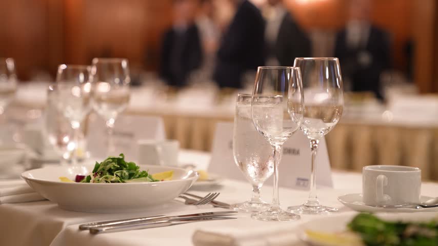 Elegant banquet dinner table setup with sparkling crystal glasses, fine dining plates, and professional catering at a luxury formal event or corporate gala.

