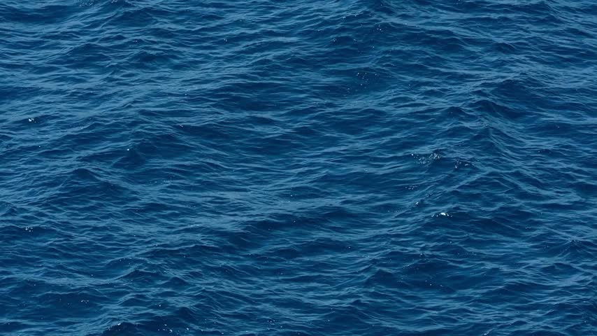 Waves blue ocean surface under reflecting sunlight. The scene captures the essence of marine beauty and the tranquility of open water under a clear sky.