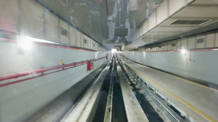 Tracking POV 4K 60fps shot from the front window of an automated aerotrain traveling through an underground concrete tunnel and emerging into the daylight at Kuala Lumpur International Airport.