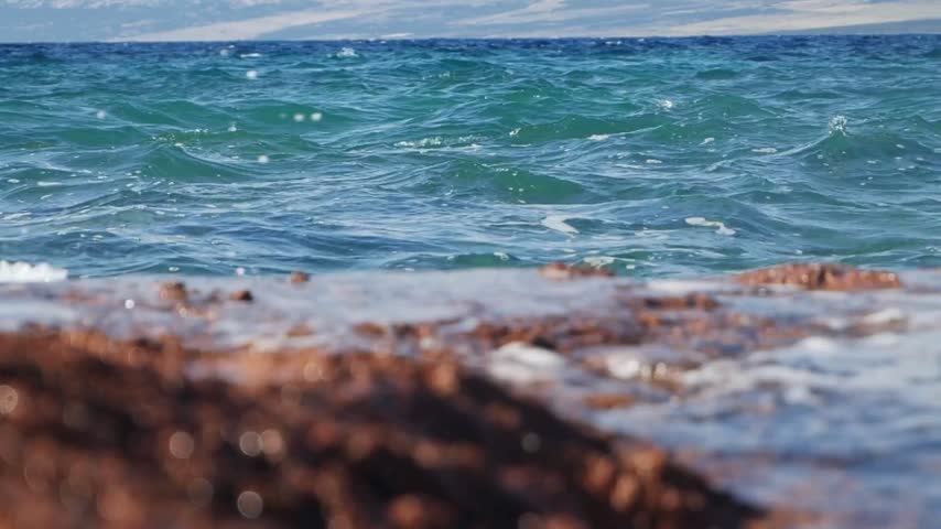 Waves crash against a rugged shoreline revealing clear blue water under bright skies, highlighting natural coastal beauty in a serene coastal environment.