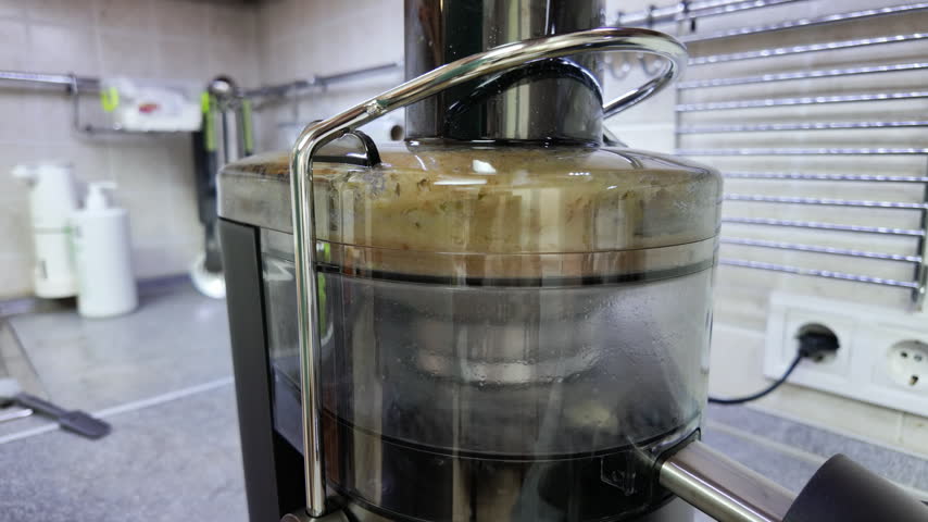 Close-up static shot of a modern electric juicer spinning and extracting juice from green apples. The transparent container accumulates pulp and liquid under bright indoor lighting on a kitchen countertop.