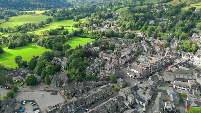 Aerial view of a quaint village nestled in lush green hills. Stone buildings cluster around winding streets. Ambleside town sits at the head of Windermere, in the lake district Cumbria UK