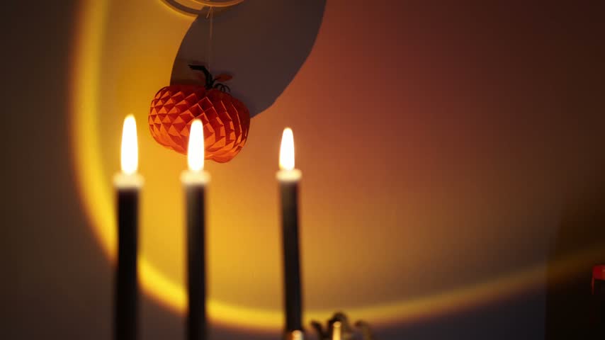 Halloween jack o lantern glows beneath tall black candles with skeleton hands and warm lights creating spooky seasonal decor and an eerie October party atmosphere at home