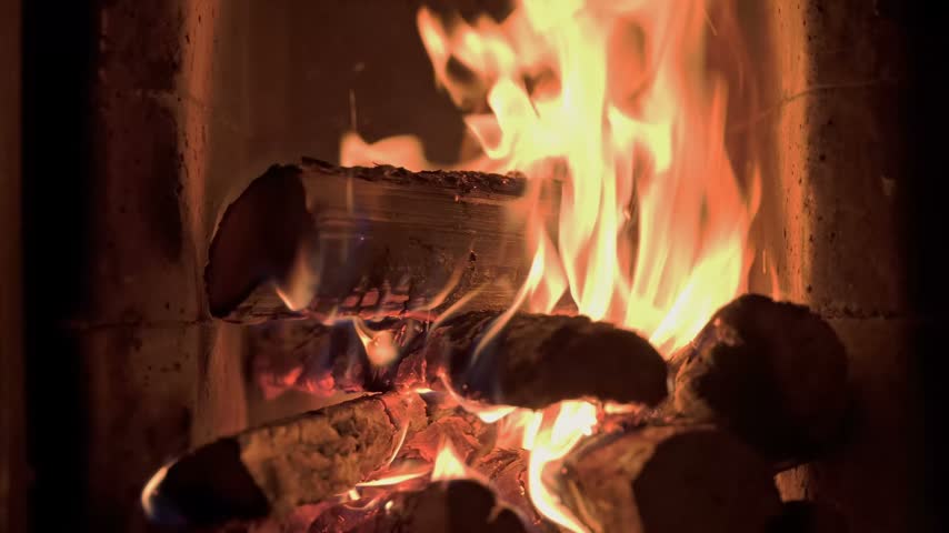 Burning wooden logs with flames and hot glowing embers inside a home fireplace. Cozy winter atmosphere and warm fire indoors.