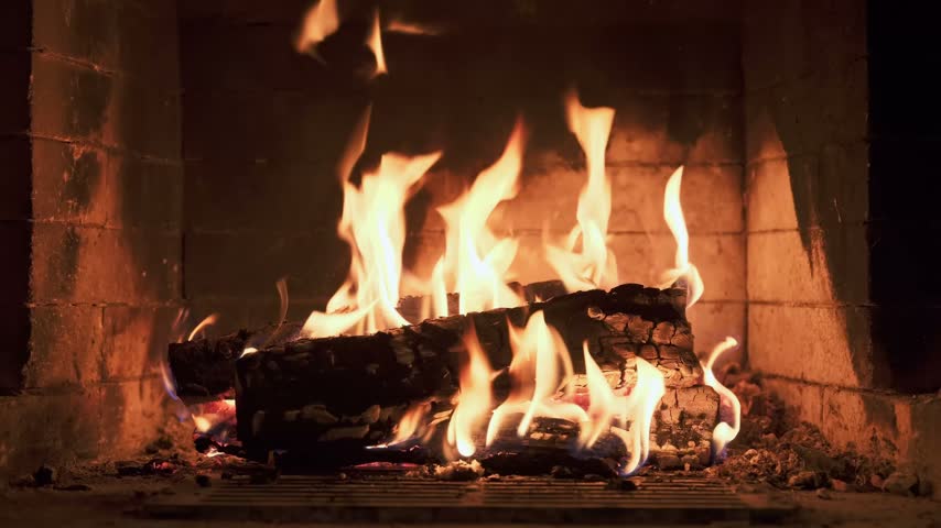 Burning wooden logs with flames and hot glowing embers inside a home fireplace. Cozy winter atmosphere and warm fire indoors.
