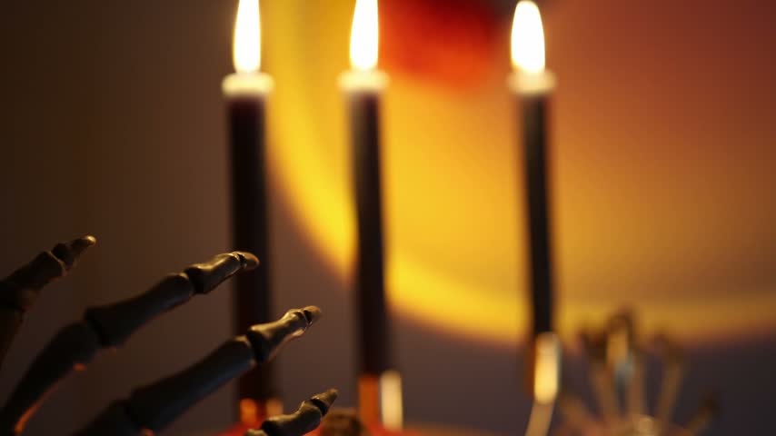Halloween jack o lantern glows among black candles and skeleton fingers creating a classic spooky decoration with warm orange light for an eerie autumn celebration inside
