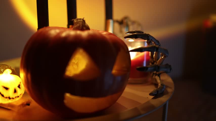 Halloween jack o lantern glows beside a creepy skeleton hand and candles creating a sinister holiday decoration with warm orange light and eerie shadows for spooky season