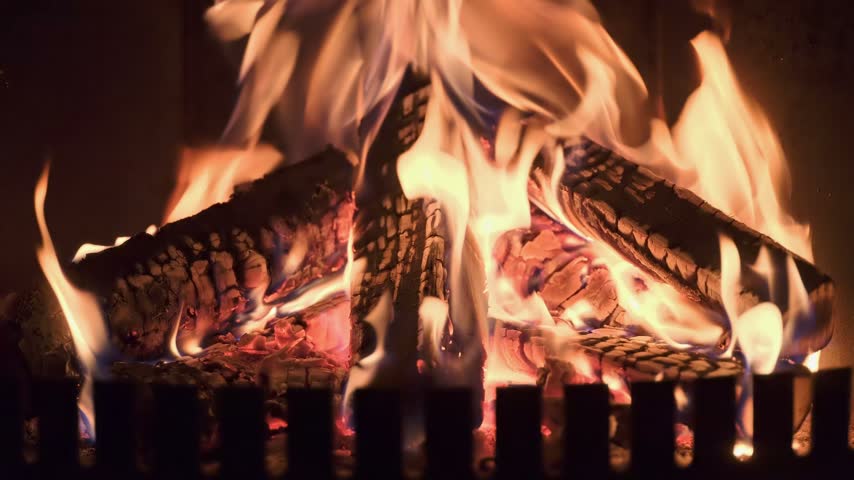 Burning wooden logs with flames and hot glowing embers inside a home fireplace. Cozy winter atmosphere and warm fire indoors.