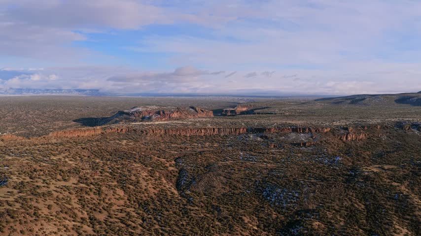 Aerial view of vast high desert canyon landscape in New Mexico featuring rocky cliffs and sparse vegetation under cloudy sky.
