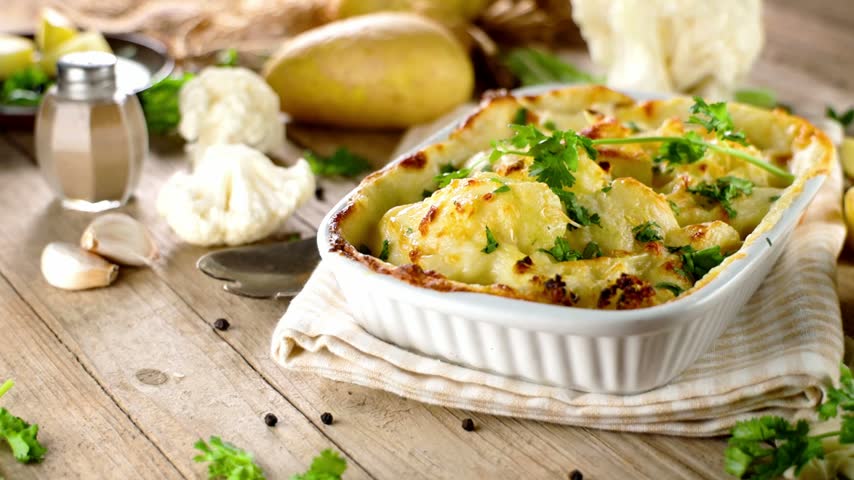Baked cauliflower and potato gratin in ceramic casserole dish on rustic wooden table