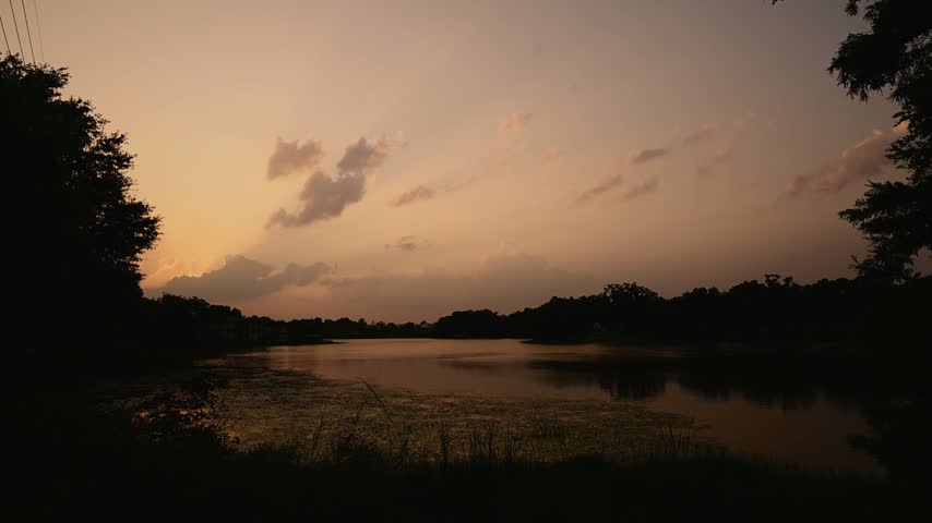 Breathtaking timelapse showing transition from golden sunset to dark twilight over calm lake water surface with tree silhouettes.