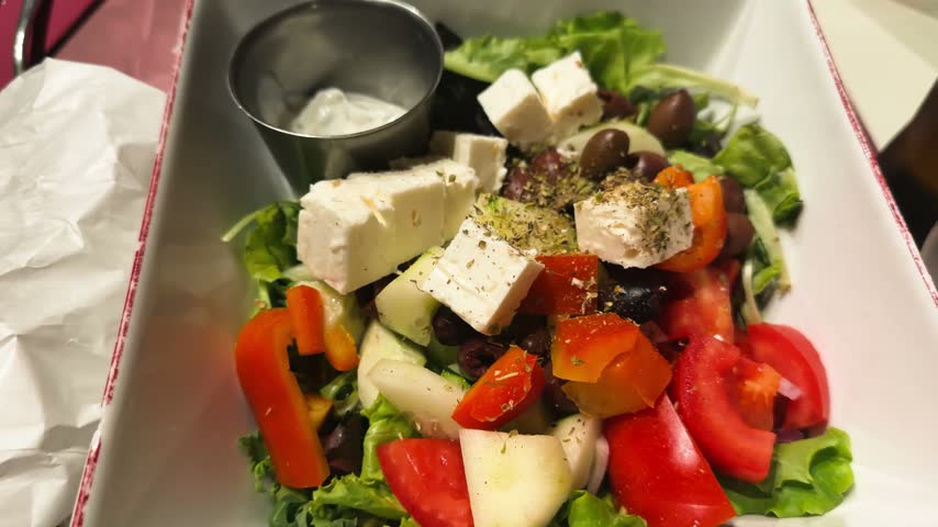 Greek salad with feta cheese, olives, tomatoes and peppers on plate, fresh Mediterranean dish, close-up food video footage.