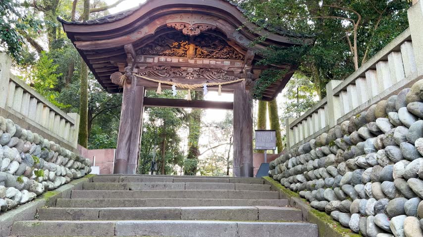 Slow motion approach towards traditional ornate wooden torii gate entrance at japanese shrine surrounded by peaceful forest landscape and historical stone walls during sunny morning.