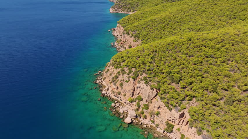 Cinematic drone shot of the pine-covered coastal cliffs of Kranidi, Greece, near Ormos Luxury Villas, where turquoise Aegean waters meet dramatic rocky shores.