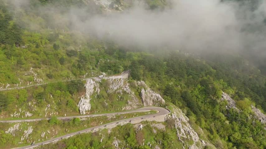 Aerial view of a winding road on a mountainside, clouds drift by.