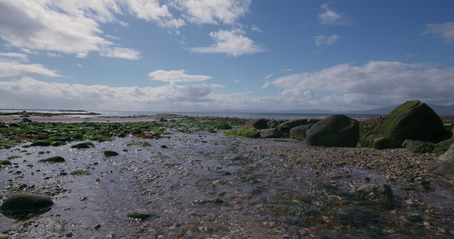 Cinematic shot of stream on sunny Scottish beach with rocks with algae 2
