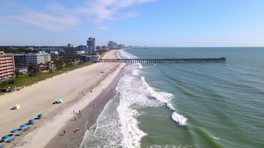 Beyond scattered beachgoers, pier pilings extend into Atlantic water along Myrtle Beach.
