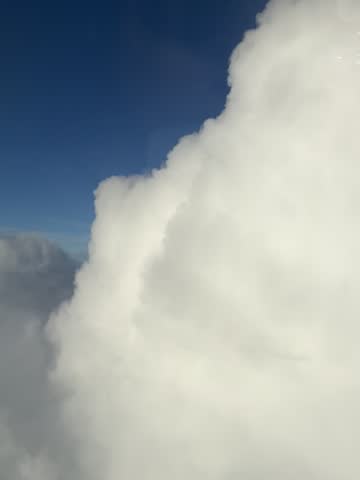 Aerial view of soft white clouds and blue sky filmed through an airplane window during a flight.