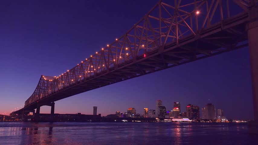 Crescent City Connection bridge over Mississippi River with evening lights illuminating New Orleans cityscape skyline view.