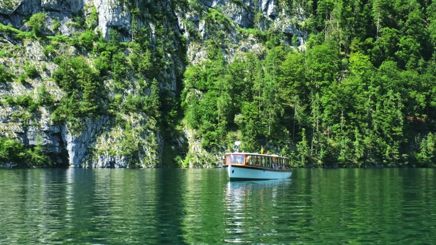 Close up of a vintage electric boat carrying tourists near the steep limestone cliffs of Konigssee lake in Bavaria, Germany.