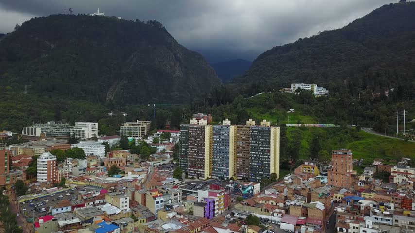 Aerial drone shot revealing dense residential area in Bogota Colombia featuring vibrant rooftops against scenic mountain backdrop.