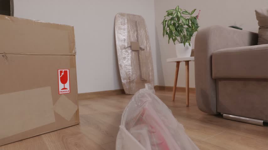 Young man carrying long rolled red area rug encased in clear plastic wrapping into apartment interior.