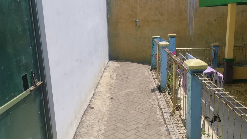 GARUT, INDONESIA - SEPTEMBER 22, 2026: A sharp corner of a narrow paving block alley next to residential houses and a small garden fence in rural West Java, Indonesia.