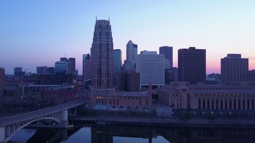 Aerial drone footage of Minneapolis city skyline at twilight showing bridge traffic over Mississippi River with urban lights.