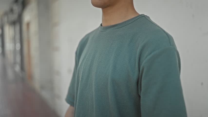 Young man with eyes closed praying with hands pressed together beside a white wall on an urban street, side profile; contemplation.