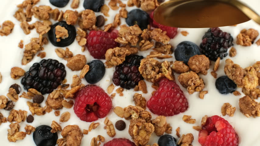 Eating Greek yogurt with granola and fresh berries, close up. Scoop with spoon yogurt with granola and fresh berries