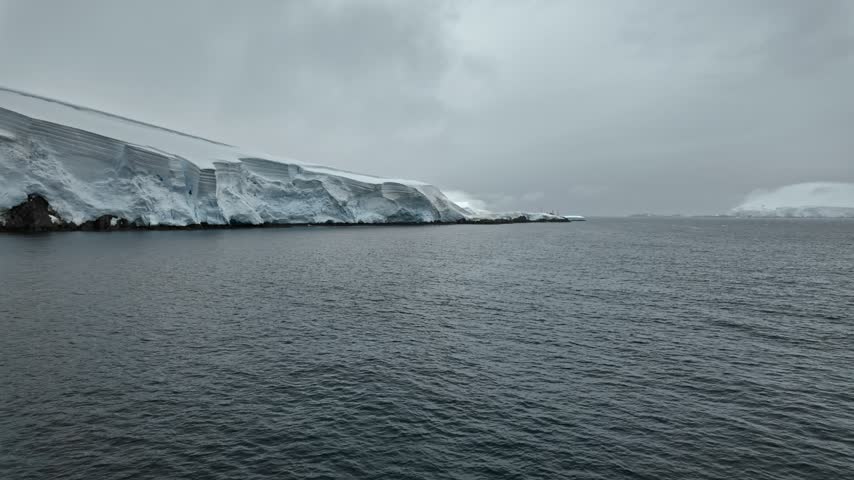 A snow-covered coastal headland tapers toward open water and a misty gap between islands in light rain.