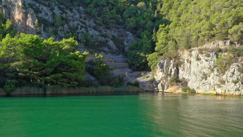 Scenic view of a turquoise river flowing through a rocky canyon with lush green pine forest and a hiking trail in Krka National Park, Croatia