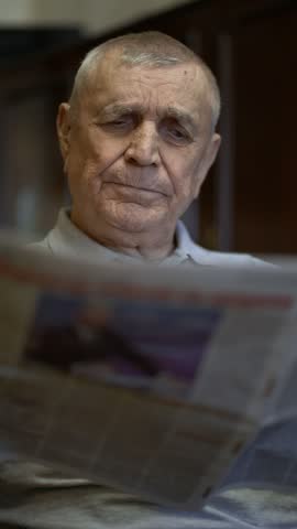 Retired elderly man reading a newspaper indoors, representing aging, leisure, news and everyday life.
