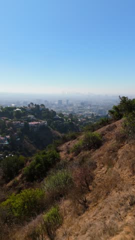 Vertical Screen: Aerial view over Hollywood Hills Los Angeles. Luxury homes on steep dry slopes above green canyon. Hazy downtown skyline on a sunny summer day. Peaceful inspiring California.