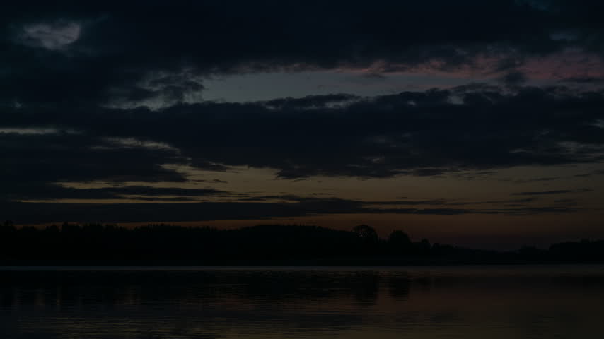 Dramatic evening sunset over a calm lake with dark clouds and forest silhouette