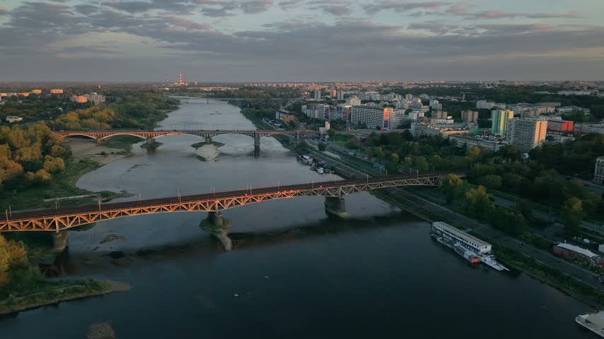 Aerial panorama of Warsaw, Poland, showing the Vistula river with bridges and the modern city skyline with skyscrapers reflecting the beautiful golden light of the setting sun