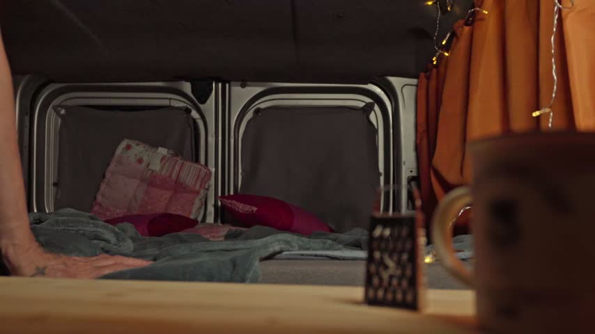 Man lying down on campervan bed turning off portable small lamp on flexible tripod mount at night.