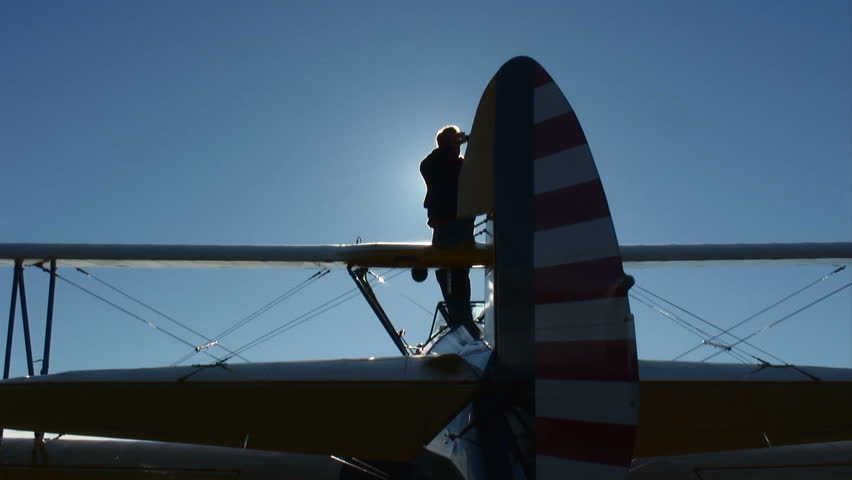 Pilot standing on a parked biplane, silhouetted against the sky.