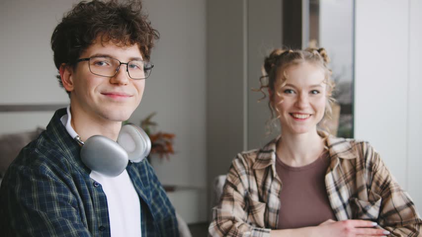 Young adults enjoy casual indoor time together while smiling at the camera in a comfortable setting with headphones around one person