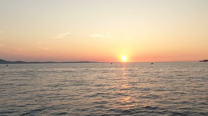 Warm orange sunset above a rippled sea with distant islands and a narrow path of reflected light across the water.