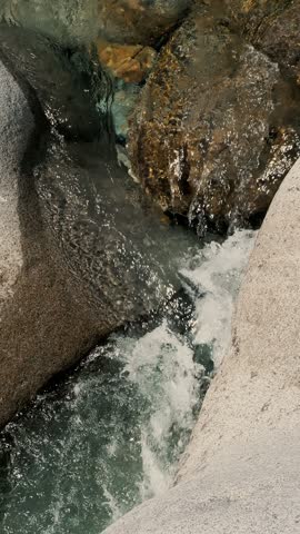 Slow-motion shot from above of alpine water rushing through tight rocky passage