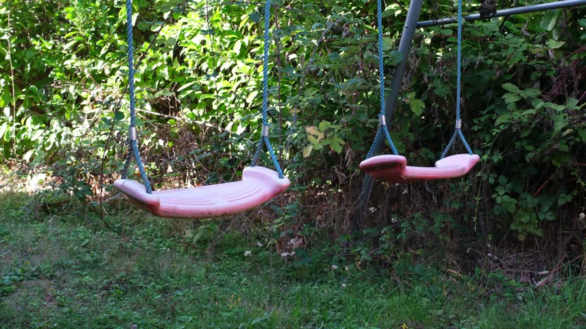 Close up of two pink plastic swings on blue rope in closed garden 
