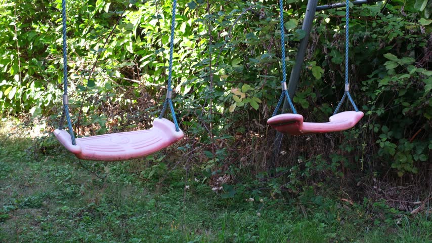 Close up of two pink plastic swings on blue rope in closed garden with one swing back and forth